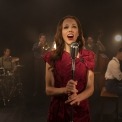 Woman in red dress singing behind a microphone in front of a band