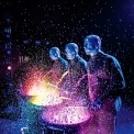 Three bald blue men dressed in black playing drums in front of a black background. Colored paint is splashing off the drums.