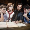 Two men and two women standing behind a piano looking at sheet music