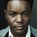 Close up shot of an African American man staring into the camera in front of a gray background.