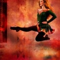 A woman in a green dress and black tights Irish dancing in front of an orange background.