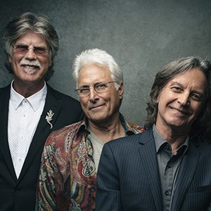 All three members of the Nitty Gritty Dirt band standing in a line in front of a gray background