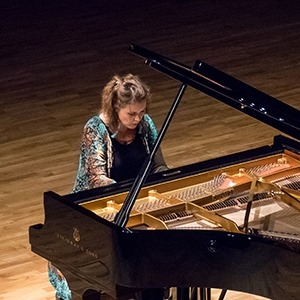 Image of Gabriela Monteri, taken from an elevated position, showing her seated at a piano in a colorful robe.