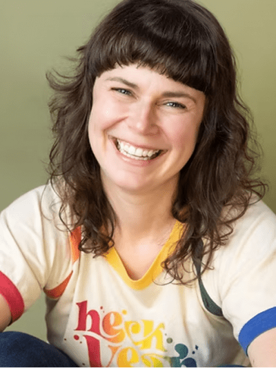 smiling woman with brown, long hair and cream top with rainbow trim