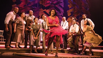 Image of a cast member dancing in a red dress while other cast watch