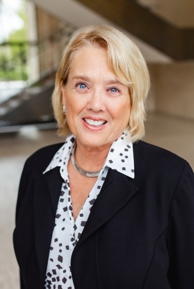 headshot of Dee Cummins. woman with short blonde hair wearing black and white shirt and black blazer