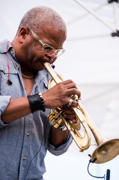 Image of a performer in a light blue shirt playing a trumpet outside at Jazz in June