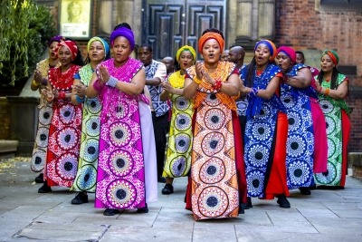 Photo of the Soweto gospel choir wearing brightly colored dresses and shirts.