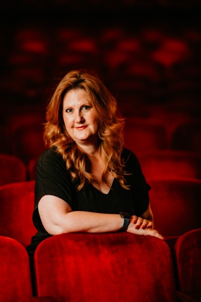 Woman with red hair with black blouse sitting in red theater seats