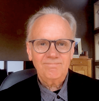 Man with glasses and grey hair smiling with black suit jacket 