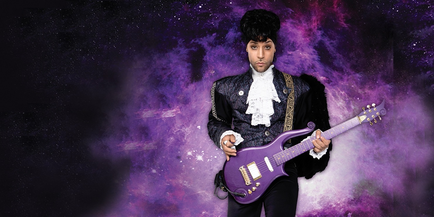 Image of a performer dressed up as Prince in a black suit and holding a purple guitar while standing in front of an image of a purple galaxy in space.