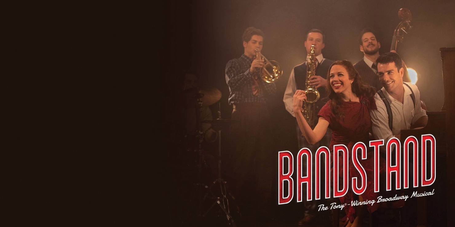 Woman in a red dress sitting next to a man at a piano with a drummer, trumpeter, a saxophonist, and an upright bassist behind them in front of a dark background.