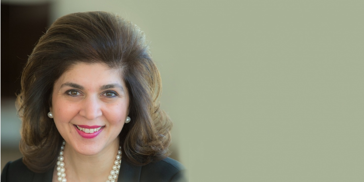 Woman with brown hair and pearls wearing a black blazer.