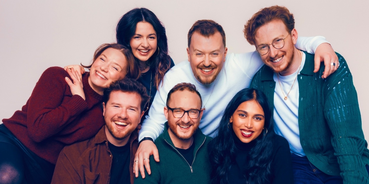 a group of seven smiling humans pose closely together on a small green loveseat