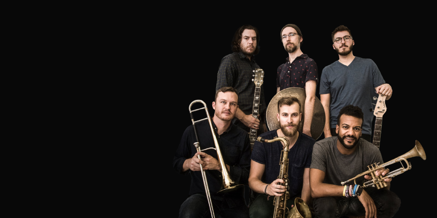 Six men look into the camera. From left to right they hold: A guitar, a cymbal, a bass guitar, a trombone, a tenor saxophone, and a trumpet.