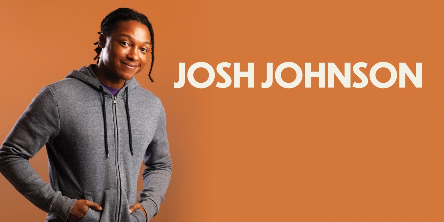 a man in grey hoodie with hands in pockets poses against an orange background