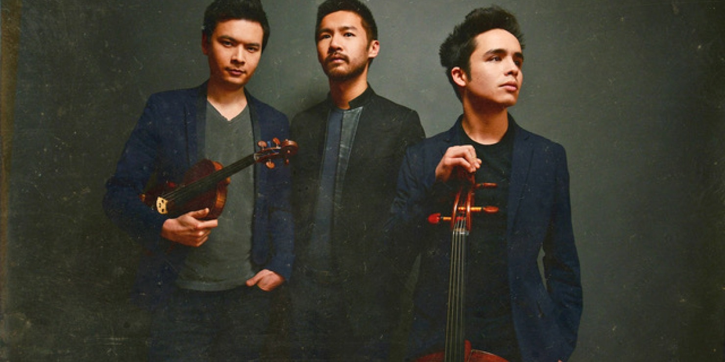 three men pose with instruments in front of a dark and moody background