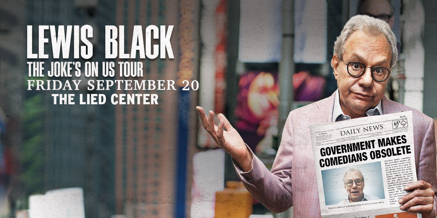 Man in pink suit holding a newspaper that reads "Government makes comedians obsolete" in front of a city background with the words "Lewis Black the Joke's On Us Tour" in white above him