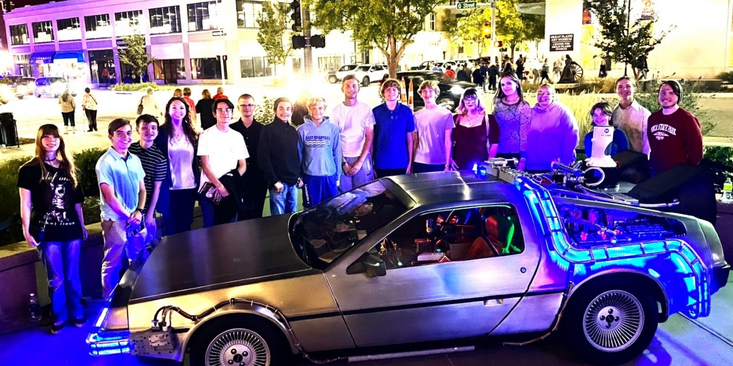 a group poses with an old relic car at night