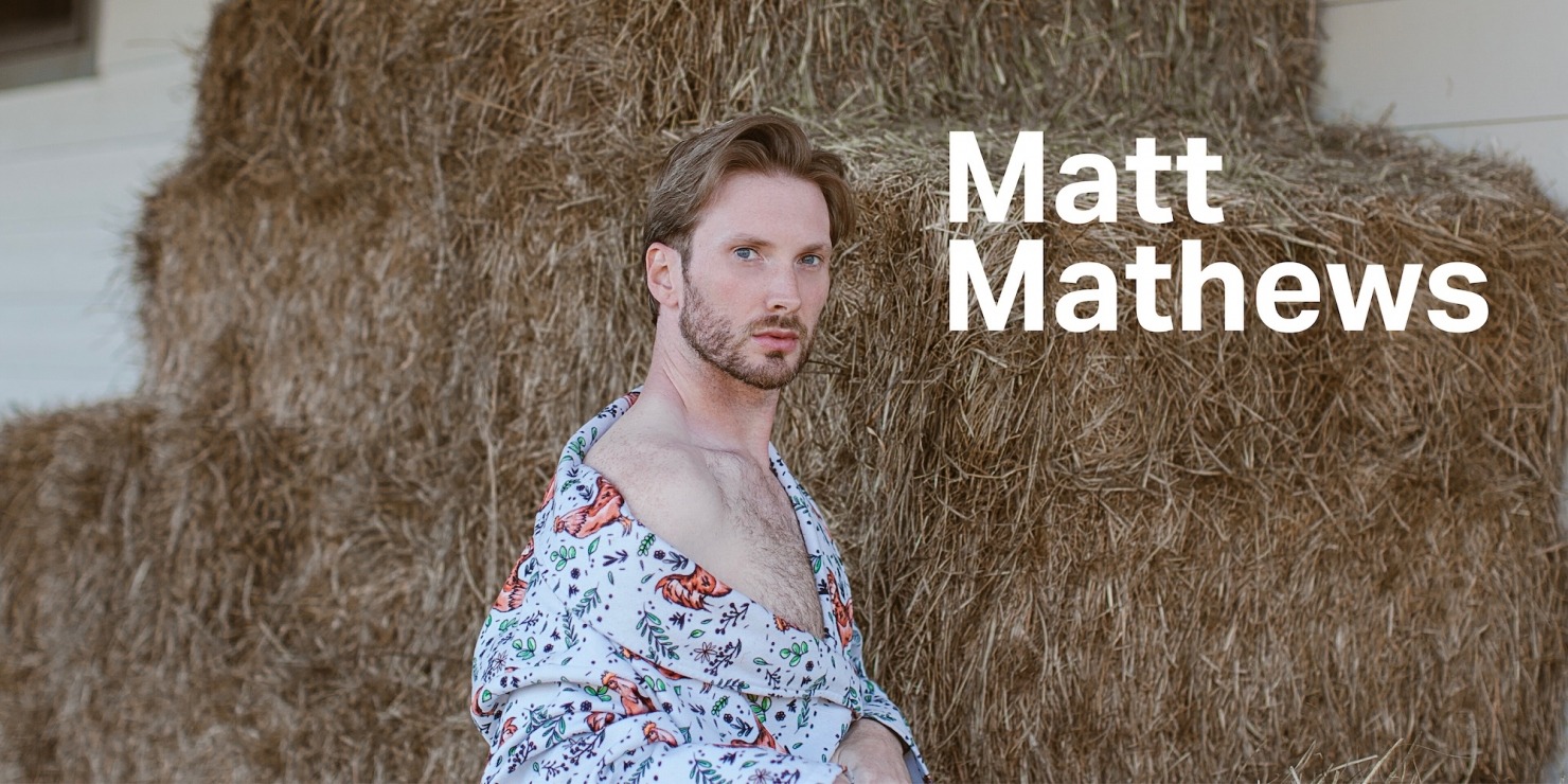 a fashionable man poses in front of hay