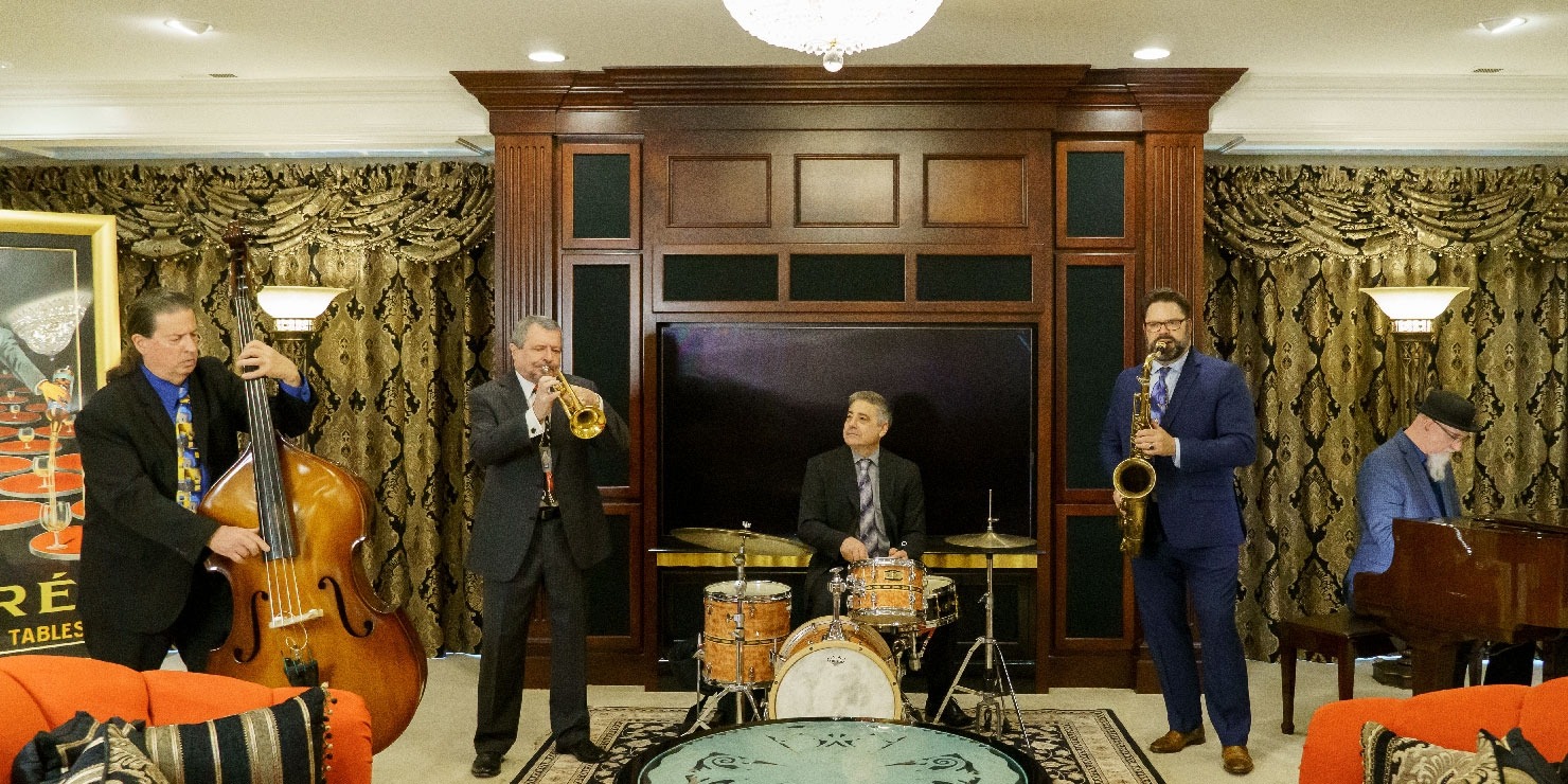 Five men standing and playing jazz instruments in a foyer area.