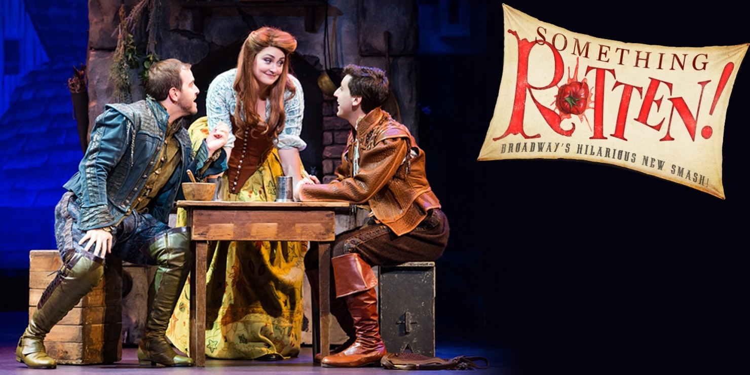 One man in a blue costume sitting at a brown table with one man in a brown costume. A woman is standing behind the table looking at them and she is wearing a white and yellow dress all in front of a blue background that has a brown tree.