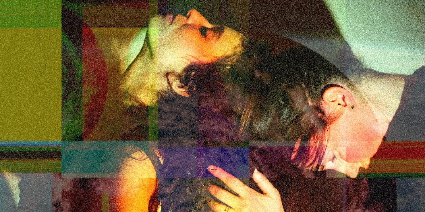 Two people sitting with one sitting in front of the other. Person in front has head leaning back while person behind is leaning forward to touch heads with person in front. Person behind is touching the hair of the person in front. There is a filter applied to the photo that makes boxes of colored filters.