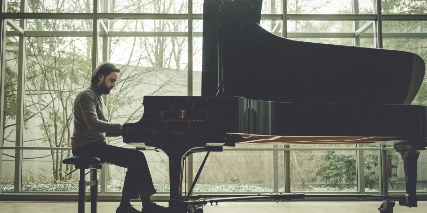 a man sits at a piano in a room with windows for walls