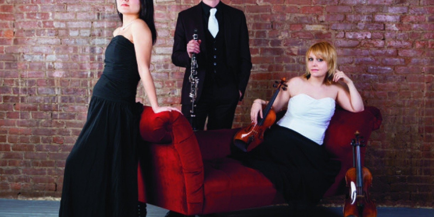 three humans in fancy attire pose together on a small red couch