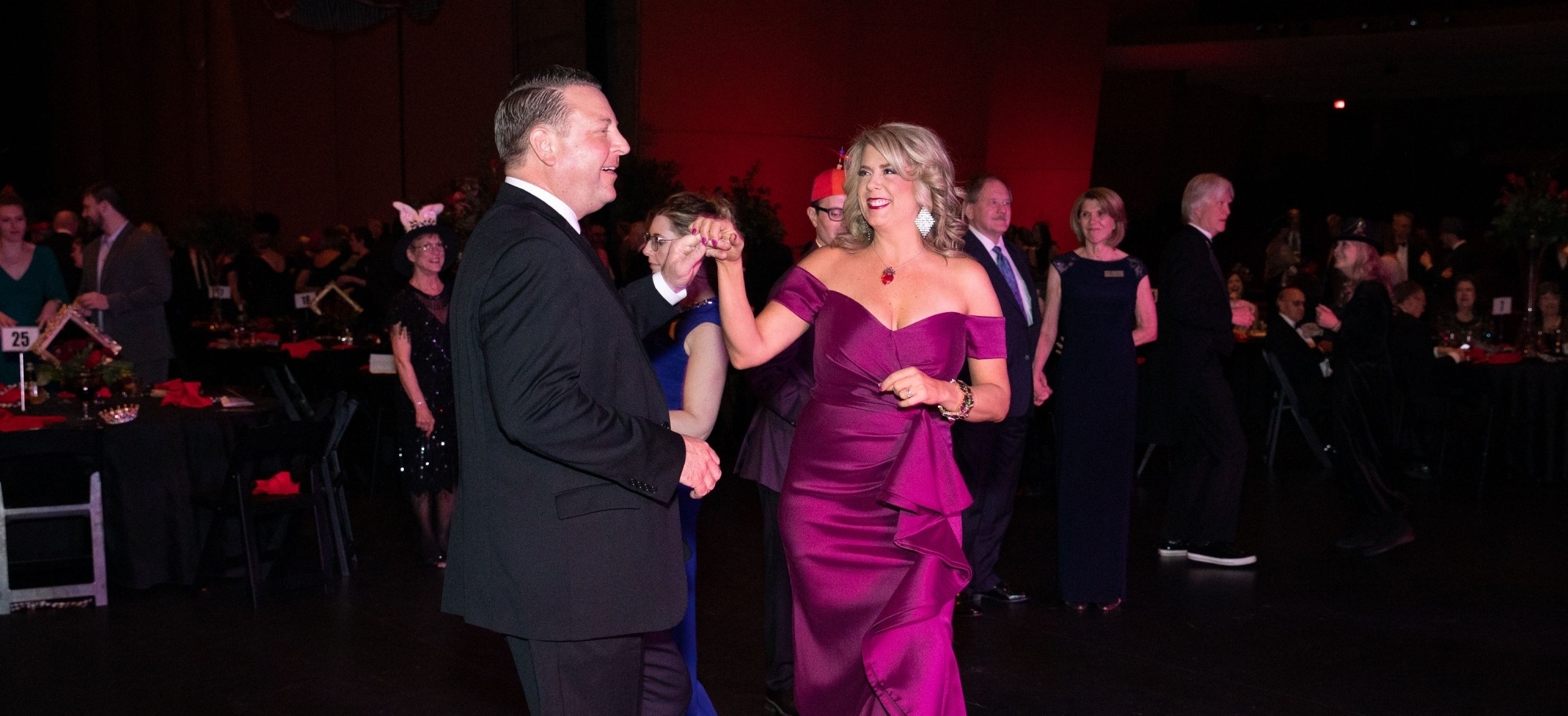 Image of a couple dancing on stage, purple dress and tuxedo. 