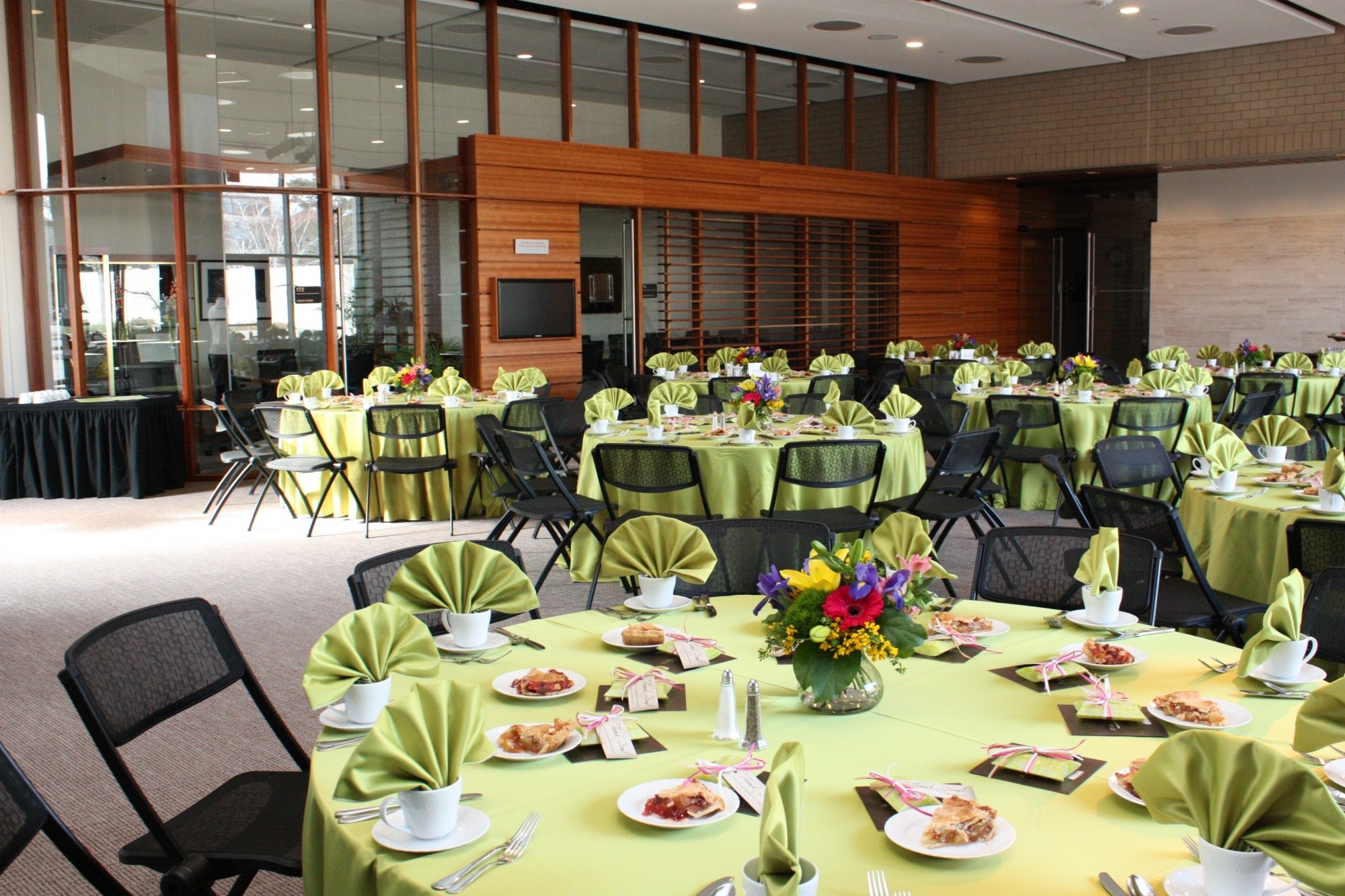 Image of the Lied Commons setup for a luncheon featuring round tables with light green linens and colorful centerpieces.