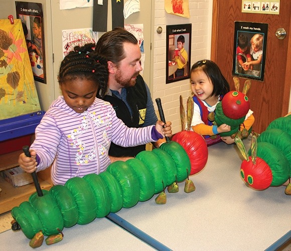 Image of two students and a performer from The Very Hungry Caterpillar playing with green and red caterpillar puppets