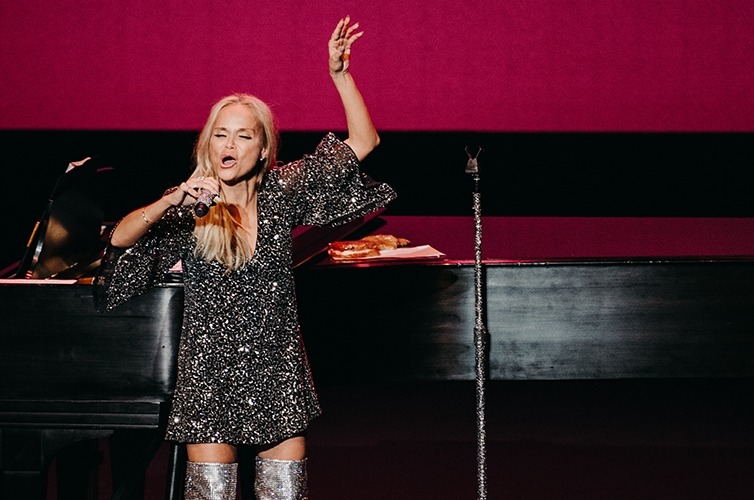 Image of Kristin Chenoweth on stage in front of a piano with arm raised singing during her Lied Center performance