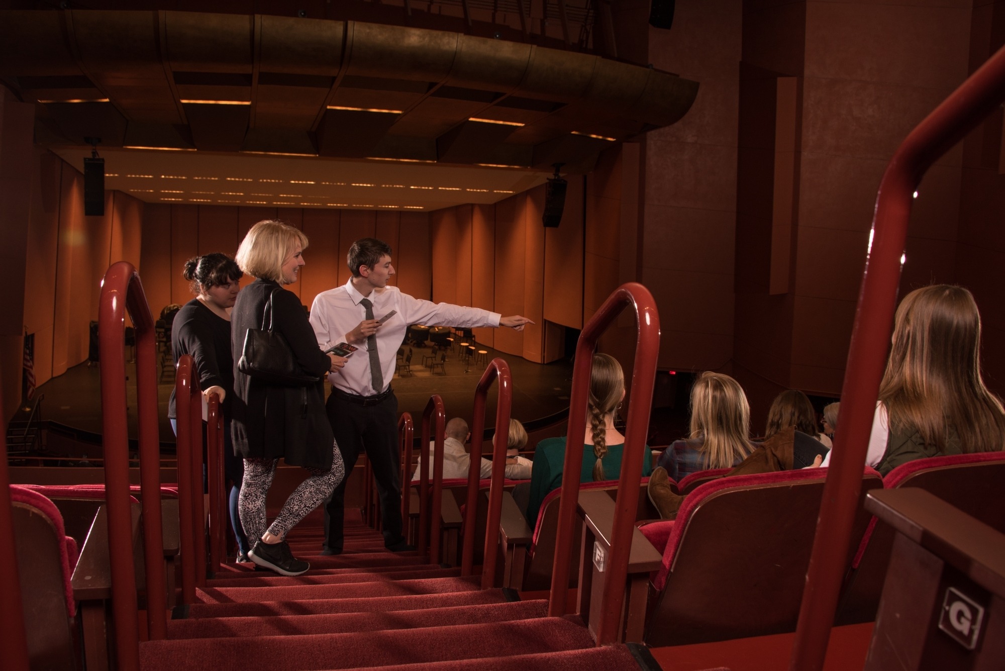 Image of an usher in a white shirt and black tie pointing guests toward their seats at the Lied Center