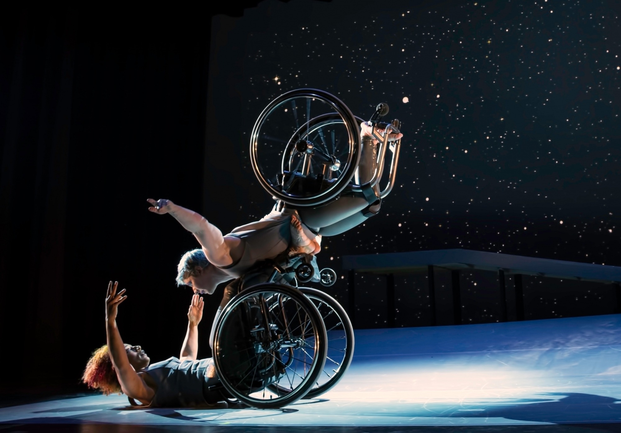 Two dancers on stage performing with wheelchairs.