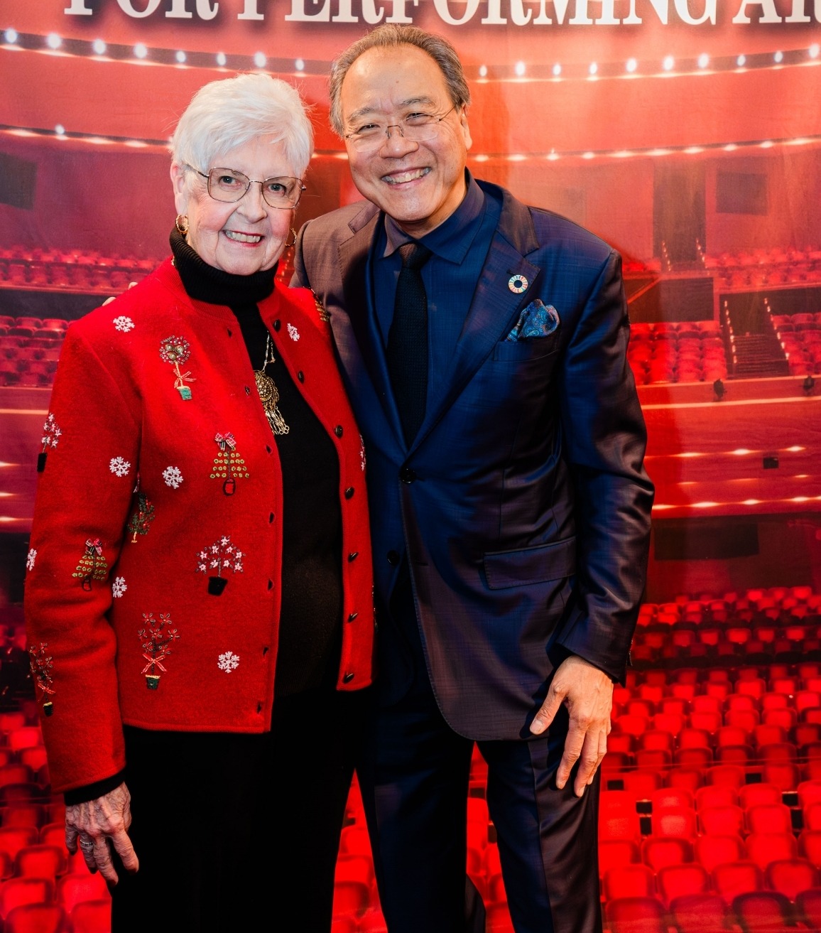 photo of anabeth cox in a red and black suite with Yo-Yo Ma in a blue suit in front of the lied center seats. 