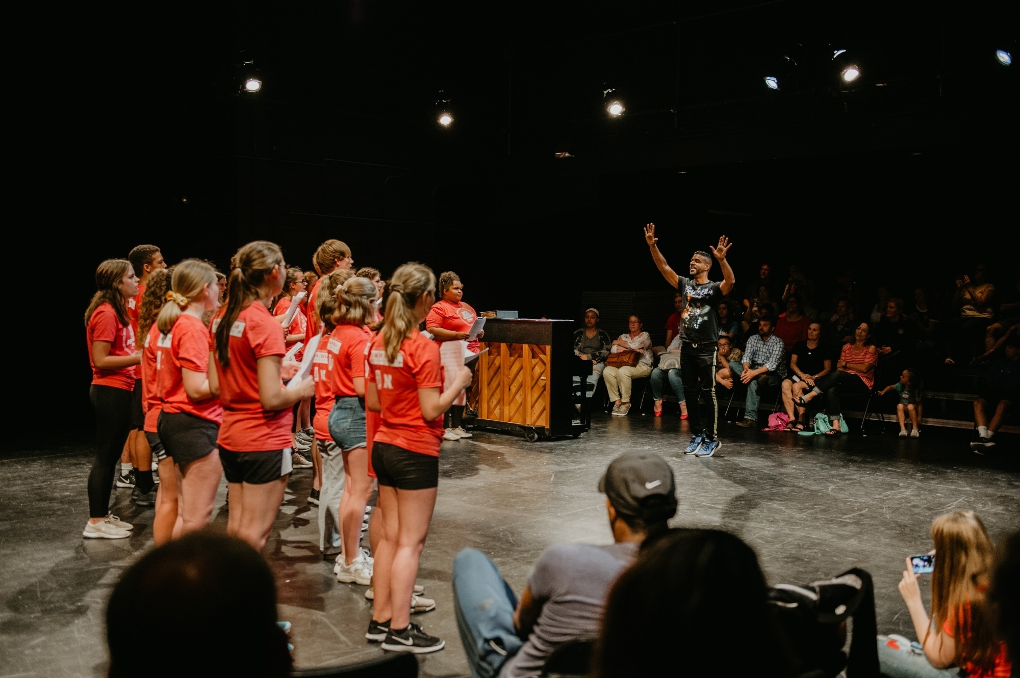 Man with black hair leading group of young people in red shirts singing