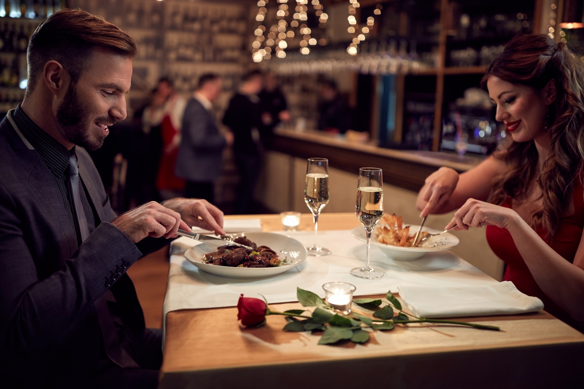 image of couple dining at restaurant with wine and a red rose on the table.
