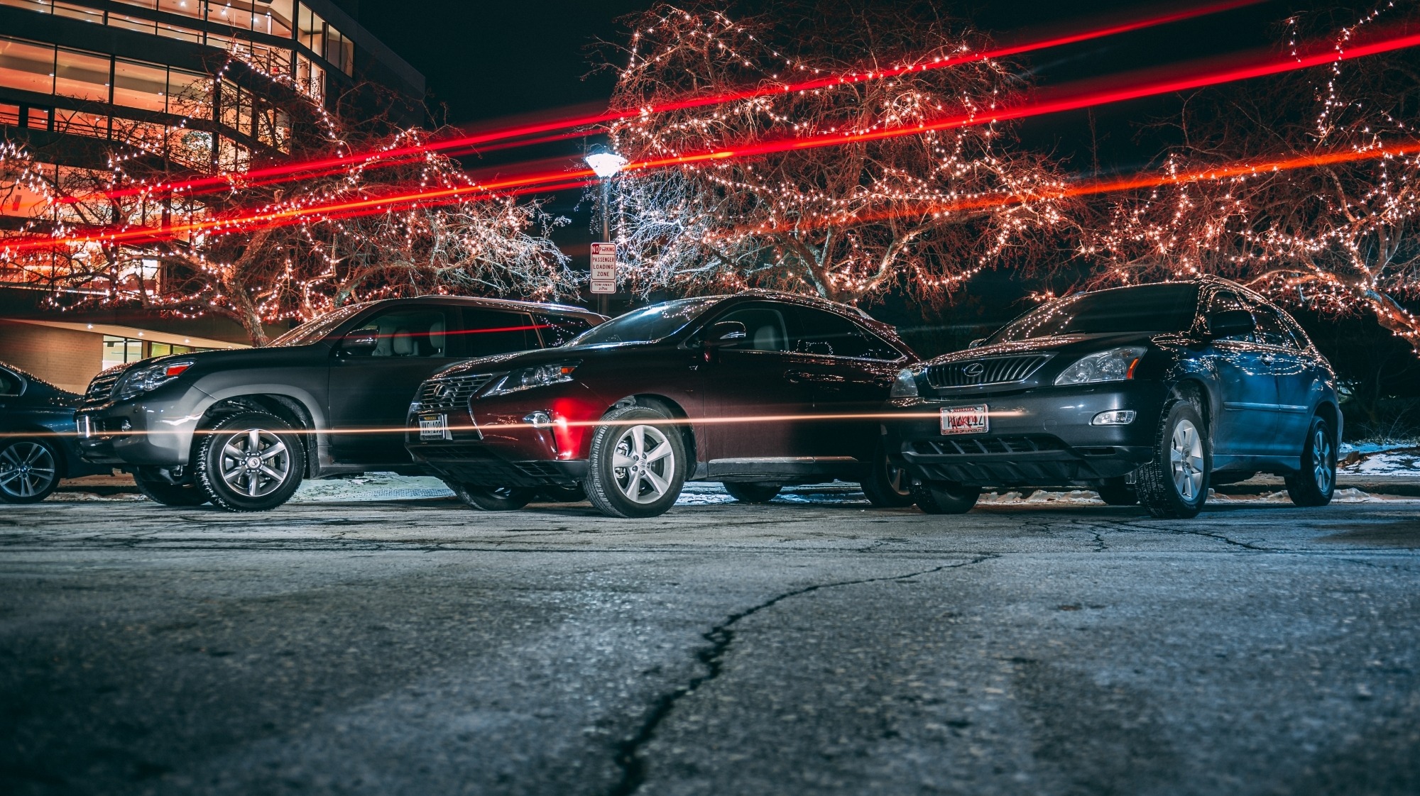 Image taken from a low angle of three vehicles parked at night in front of the Lied Center with lights streaking across the picture