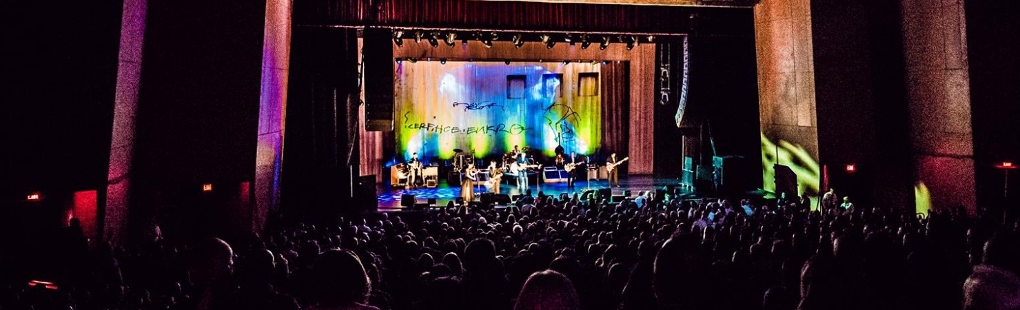 Image from the back of the hall looking at the Lied Center stage lit up in pastel colors during the John Mellencamp concert