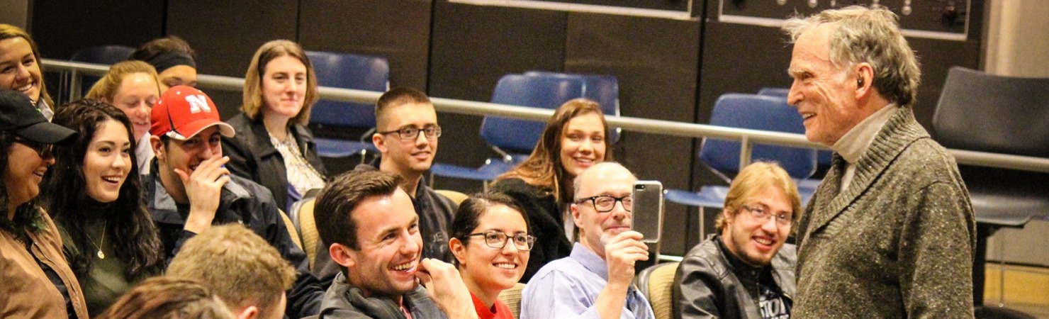 Image of Dick Cavett standing at the front of a classroom full of UNL students laughing during a lecture for journalism students