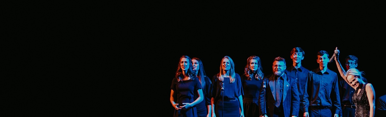 Image of local high school students on the Lied Center stage standing in front of microphones while Kristen Chenoweth holds her microphone up in the air