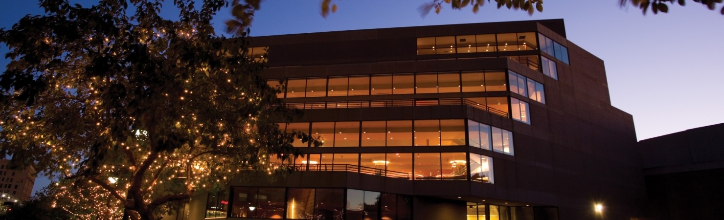 Image of the Lied Center building at night taken from street level looking up at the lights shining through the windows 