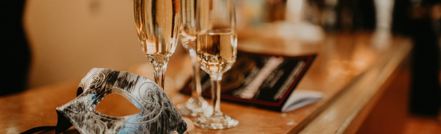 Image of a masquerade mask on a pink marble bar next to champagne flutes and a program for the Friends of Lied Gala