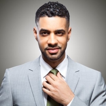 Photo of Jason Michael Webb in a gray suit adjusting a black tie