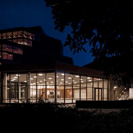 Image of the Lied Commons building taken outside at night looking in through the windows with the lights on at night