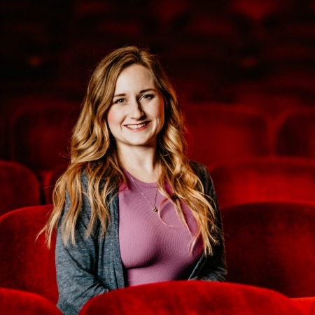 Woman with long brown hair in purple blouse sitting in red theater seats