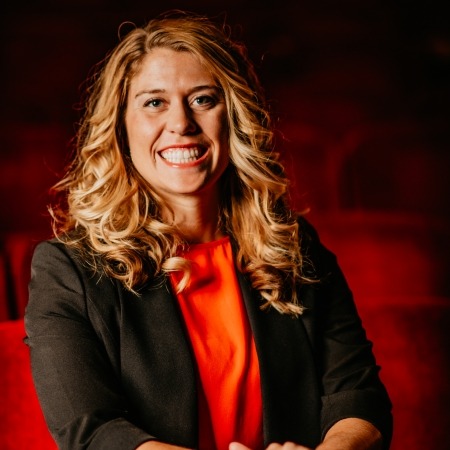 Woman with dirty blonde hair with a black blazer and red blouse