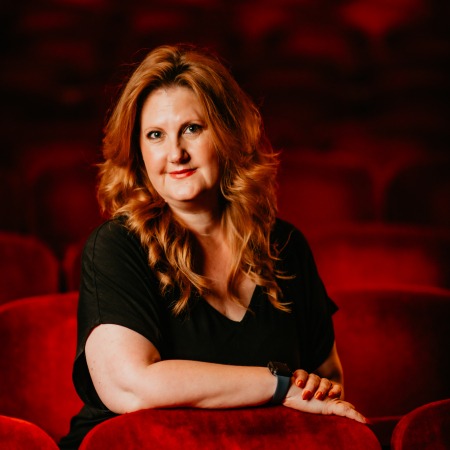 Woman with red hair with black blouse sitting in red theater seats